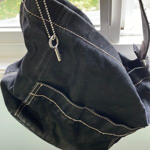 Black canvas material shoulder bag with one outside pocket. A zipper on top